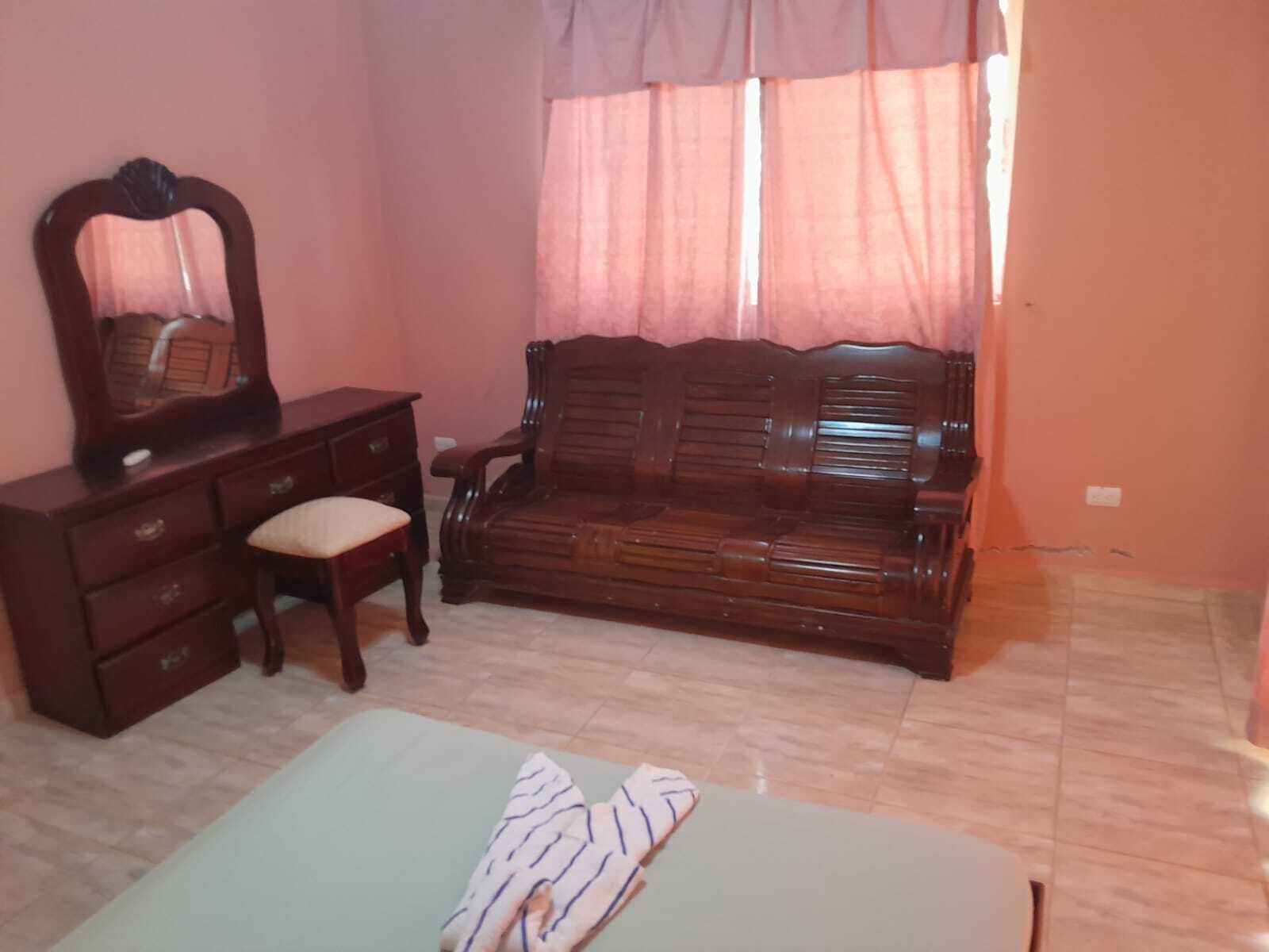 Ein Schlafzimmer mit einem Holzkoffer, einer Bank, einem Bett und einem Fenster mit Vorhängen.