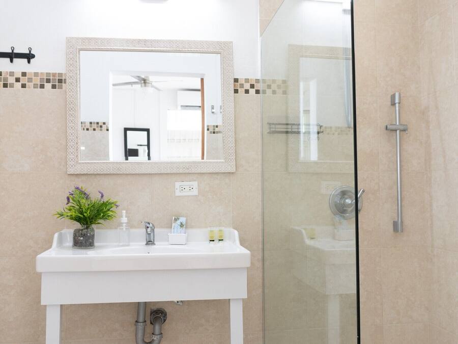 Um banheiro com pia branca, espelho e chuveiro com box de vidro.