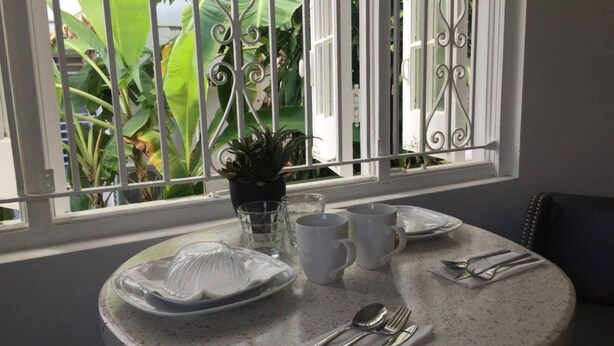 A round dining table with a glass plate, white mugs, and cutlery set. - Casa Isabel Bed & Breakfast (San Juan)