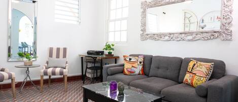 Un salon avec un canapé gris, des fauteuils à rayures, une table basse et un grand miroir décoratif.
