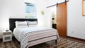 Un dormitorio con cama, mesita de noche, ventana, puerta y suelo estampado.