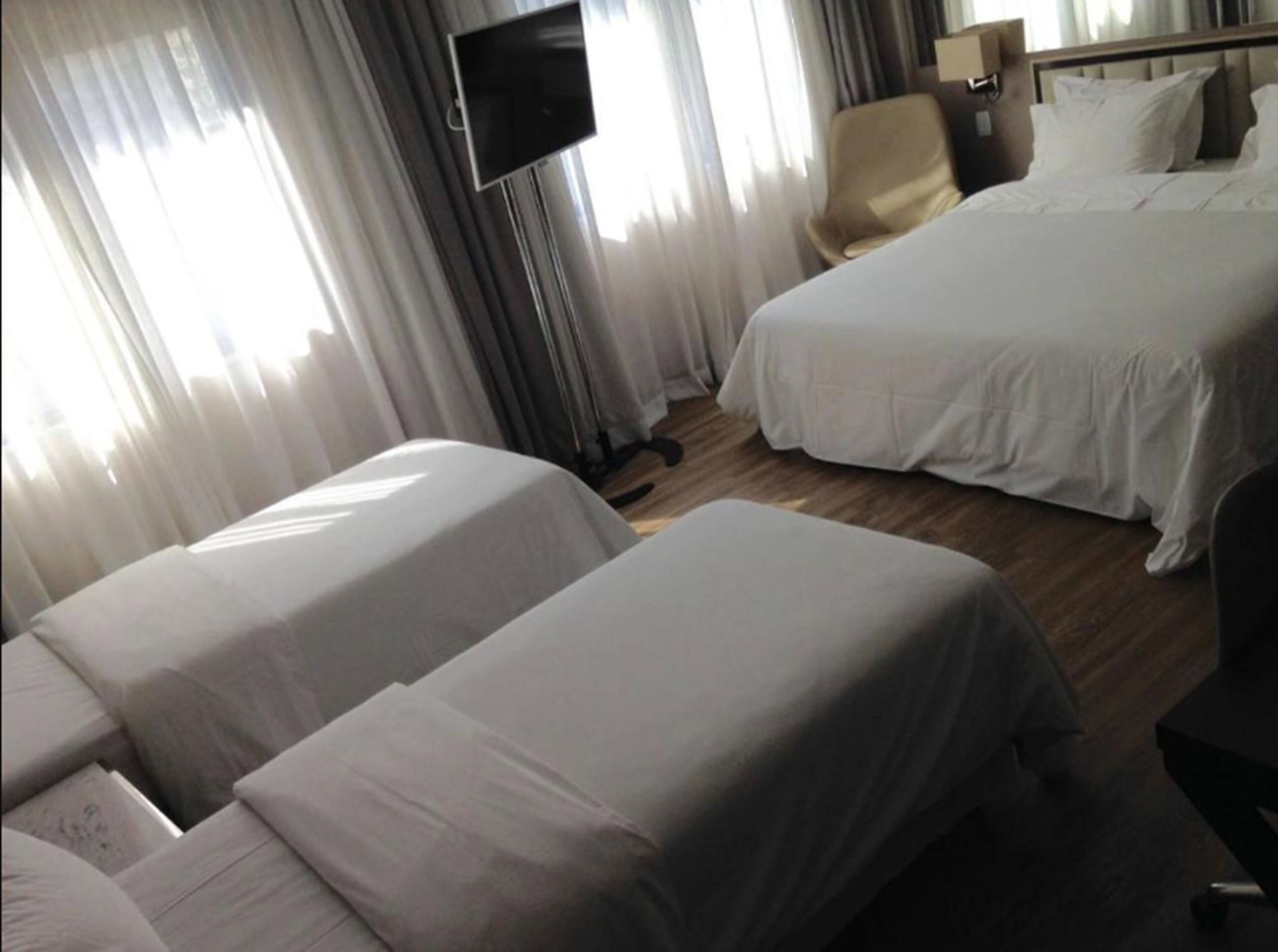A hotel room with two beds, a TV mounted on the wall, and a chair.