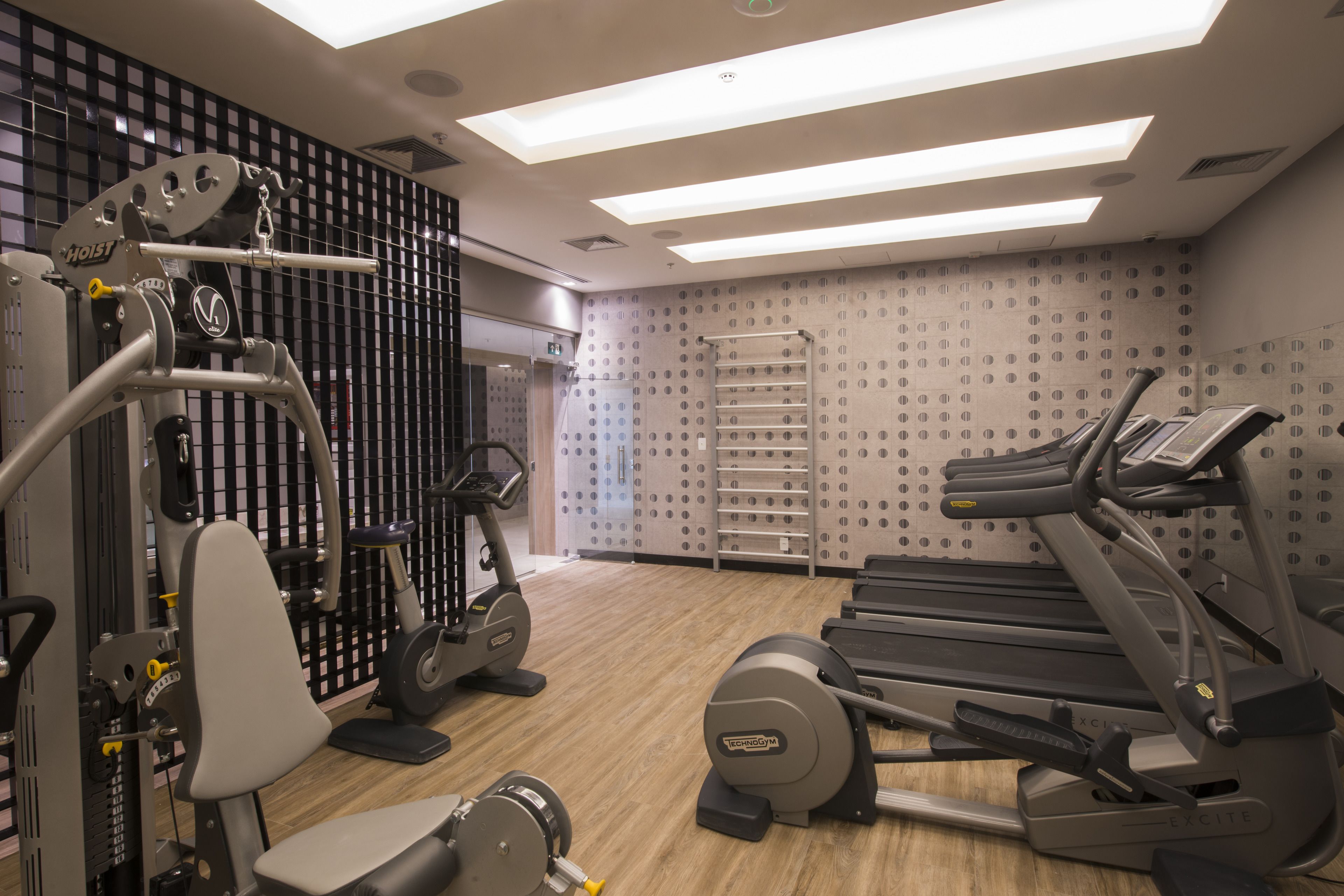 Een moderne sportschool met diverse fitnessapparaten, waaronder loopbanden en krachttoestellen, en een behang met een patroon.