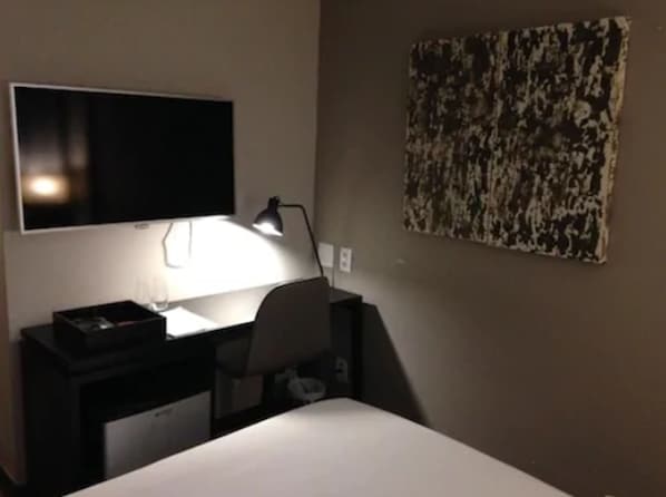 A hotel room with a bed, a desk with a lamp, a flat-screen TV, and a painting on the wall. - Hotel Atlântico Prime (Rio de Janeiro)