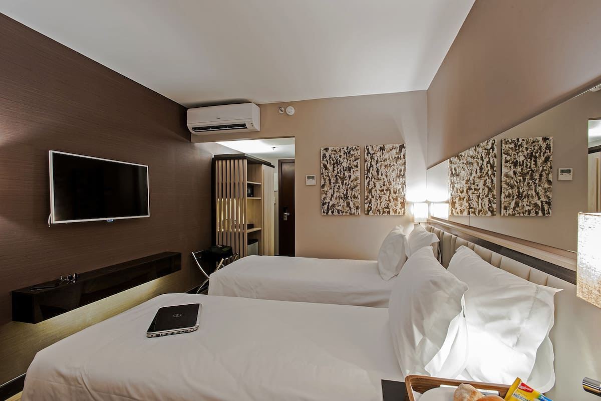 Quarto de hotel com duas camas, televisão de tela plana, ar condicionado e obras de arte nas paredes.