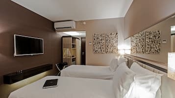 Quarto de hotel com duas camas, televisão de tela plana, ar condicionado e obras de arte nas paredes.