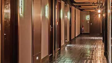 Un corridoio d'hotel con pavimento in legno, porte e una lampada moderna.