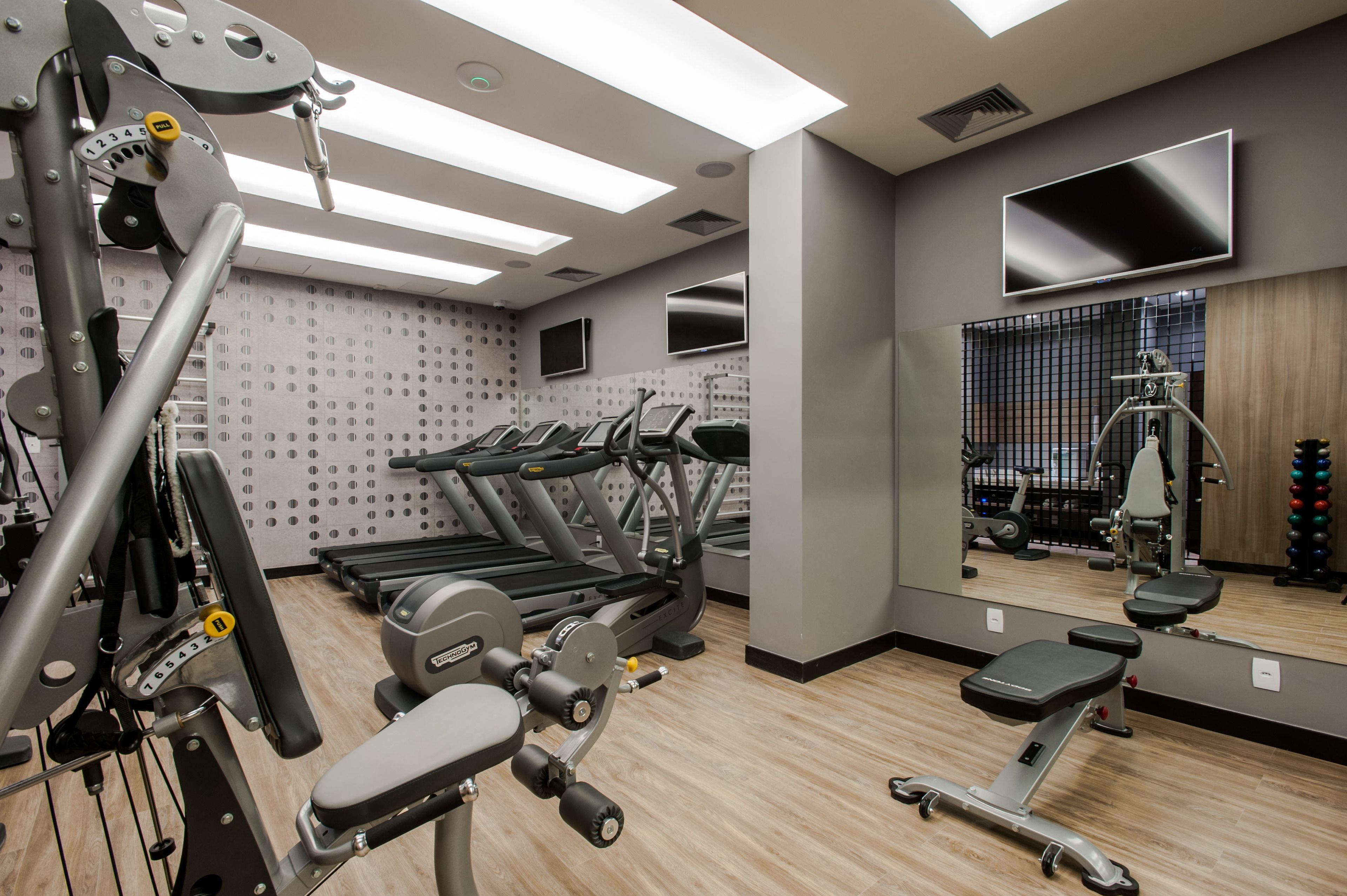 Un gimnasio moderno con cintas de correr, máquinas de pesas y un espejo grande que refleja el equipo.