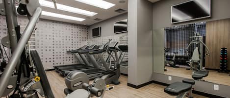 Un gimnasio moderno con cintas de correr, máquinas de pesas y un espejo grande que refleja el equipo.