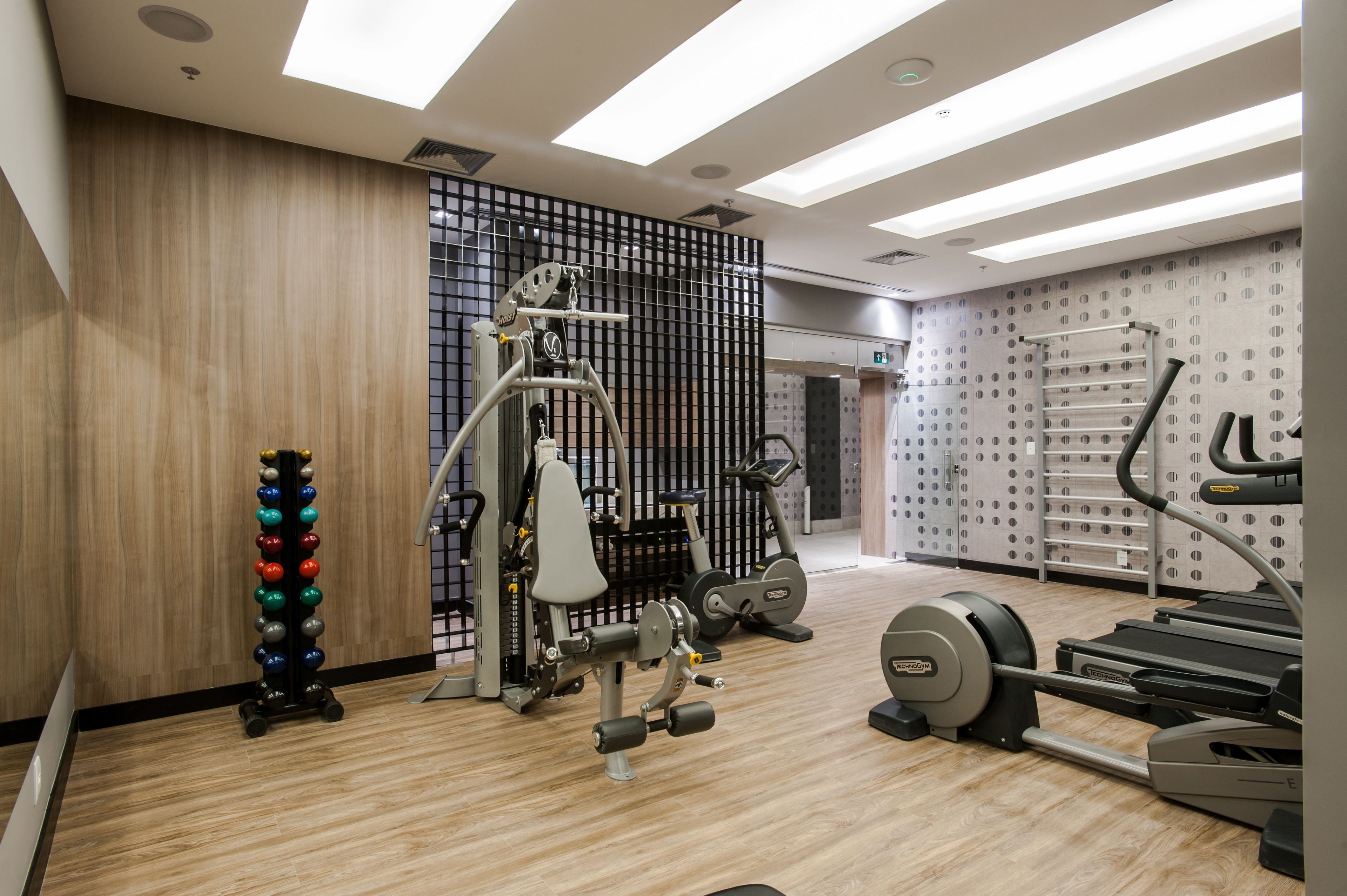 A modern gym with various exercise equipment, including a weight machine, treadmills, and a wall-mounted rack.