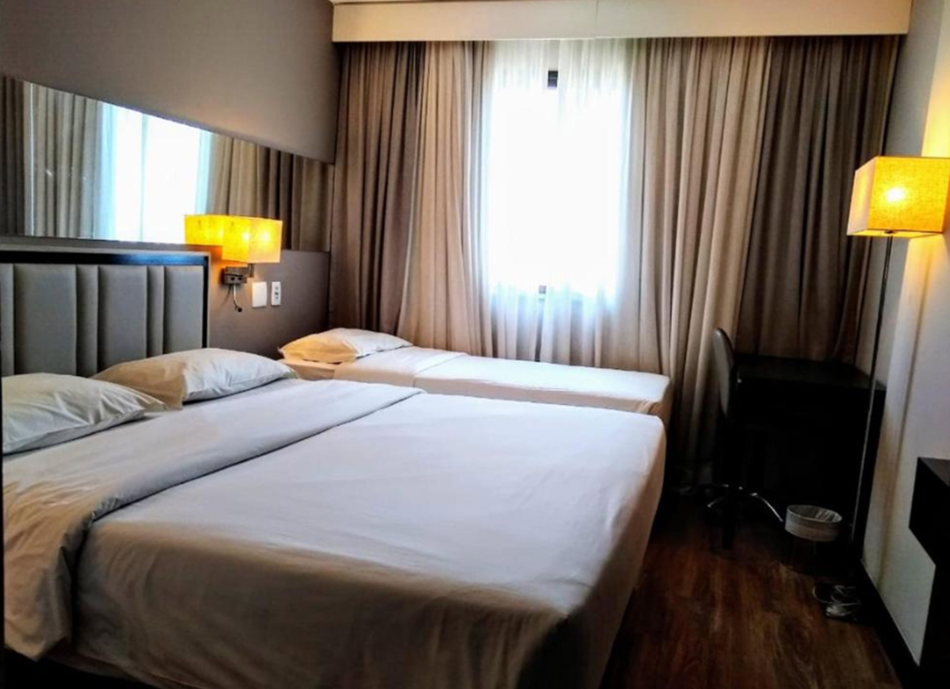 Quarto de hotel com duas camas, cabeceira, escrivaninha e uma cadeira.