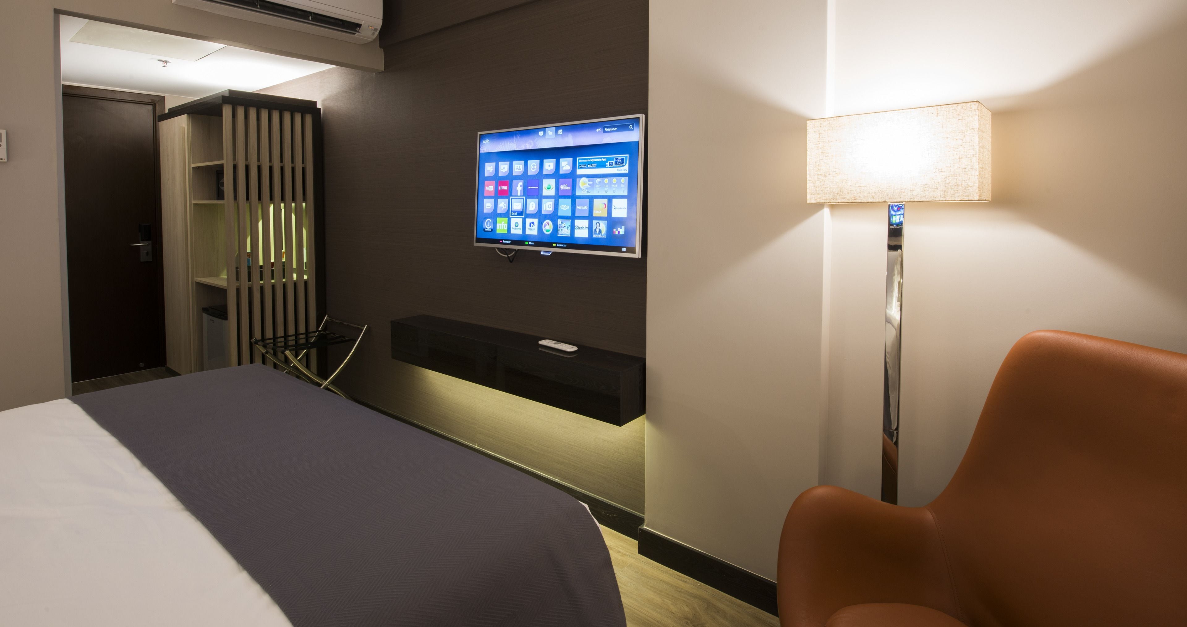 Ein Hotelzimmer mit Bett, Schreibtisch, Computerbildschirm, Stuhl und Wandfernseher.