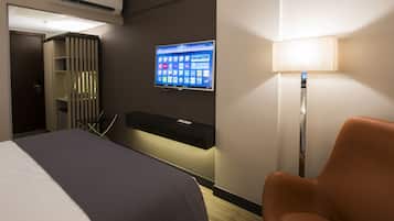 Quarto de hotel com uma cama, uma mesa com monitor de computador, uma cadeira e uma televisão fixada na parede.