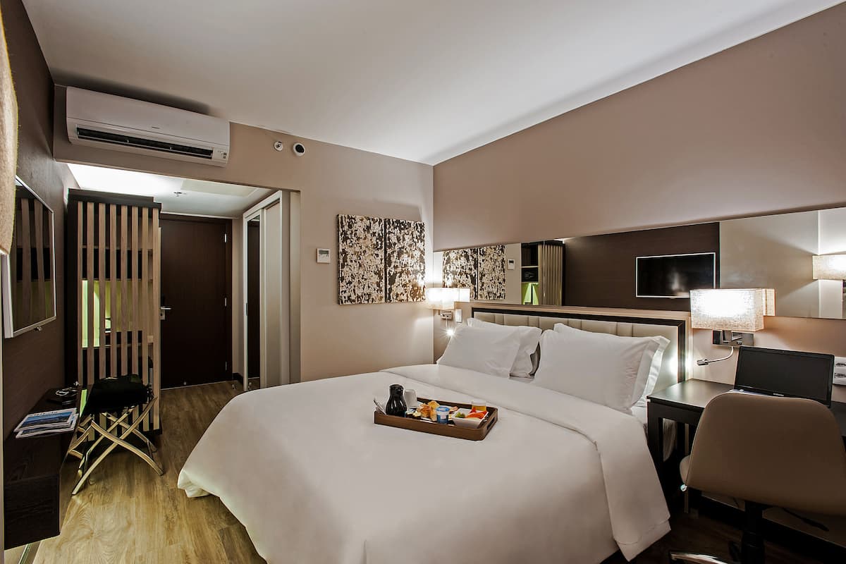 Quarto de hotel com cama, escrivaninha, cadeira e bandeja com itens de café da manhã.