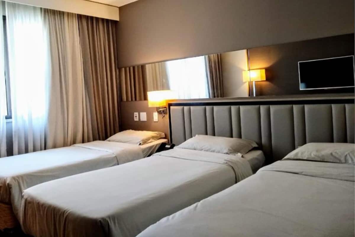 Quarto de hotel com duas camas, um espelho grande, televisão de tela plana e uma janela com cortinas.
