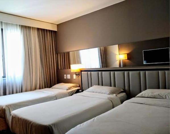 Quarto de hotel com duas camas, um espelho grande, televisão de tela plana e uma janela com cortinas.