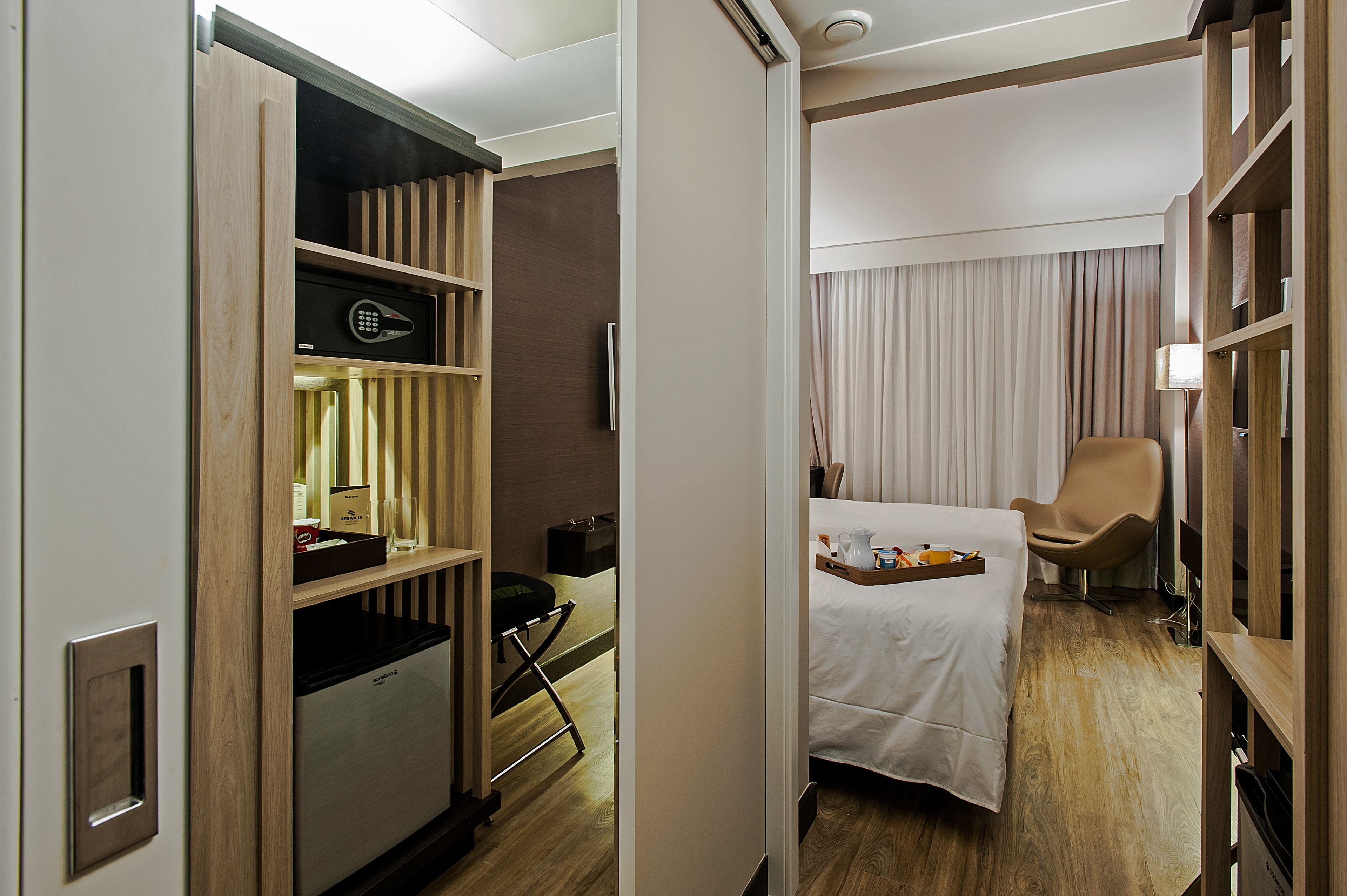 Habitació d'hotel amb un llit, una cadira, un servei de lleure amb menjar per esmorzar, un minibar i un panell de control.