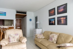 Una sala de estar con un sofá color beige, un sillón a juego, y una zona de comedor con una mesa y sillas de madera.