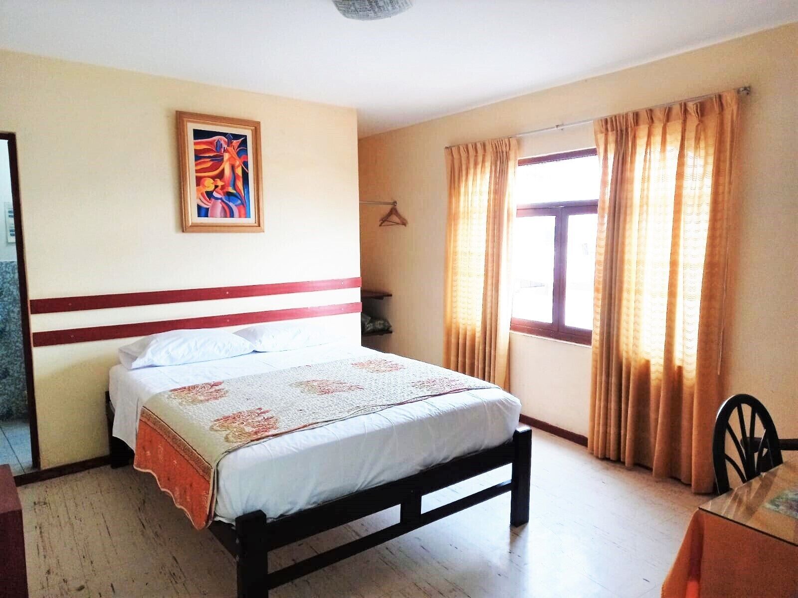 A bedroom with a bed, a painting on the wall, a window with curtains, and a chair.