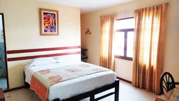 A bedroom with a bed, a painting on the wall, a window with curtains, and a chair.
