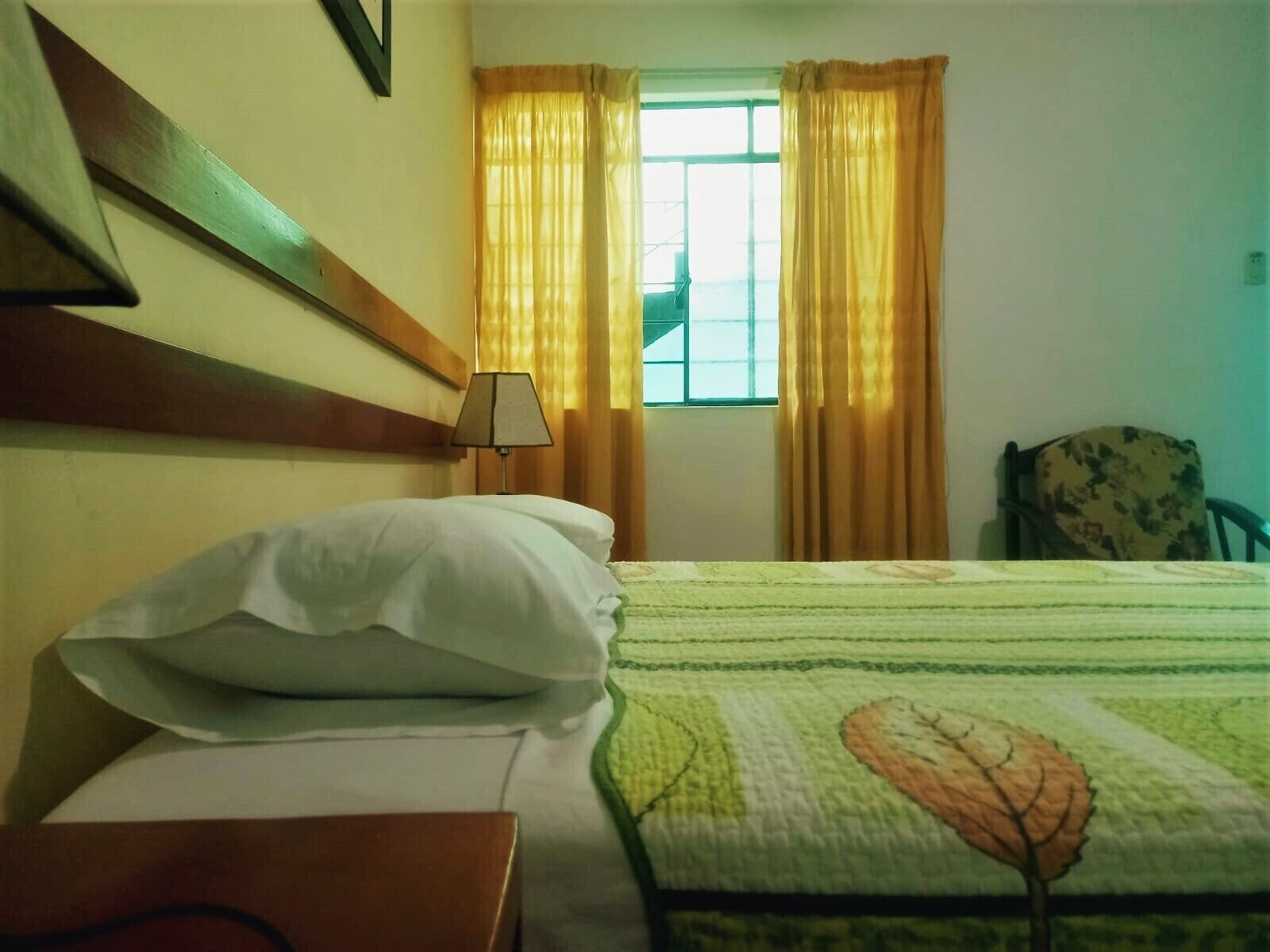 Une chambre d’hôtel avec un lit, une table de chevet, une lampe, une chaise et une fenêtre avec des rideaux.