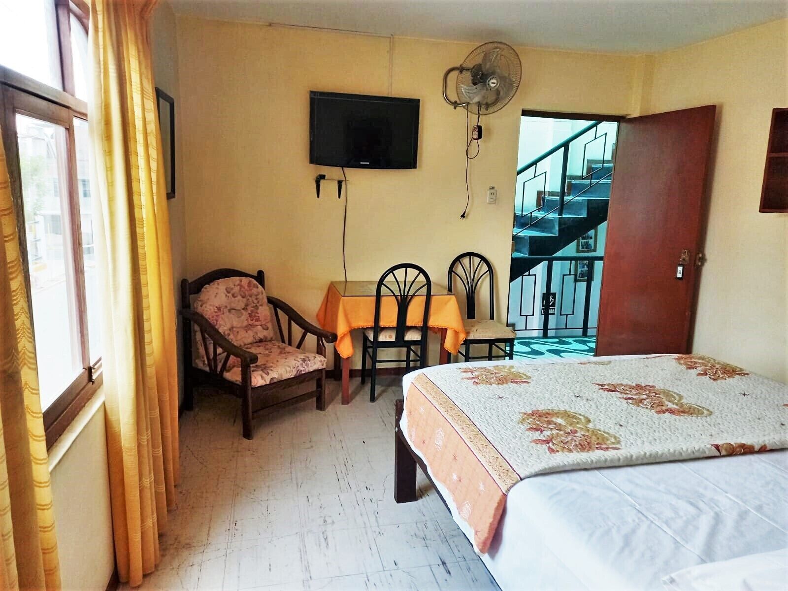 A bedroom with a bed, a chair, a table, a TV, and a staircase.