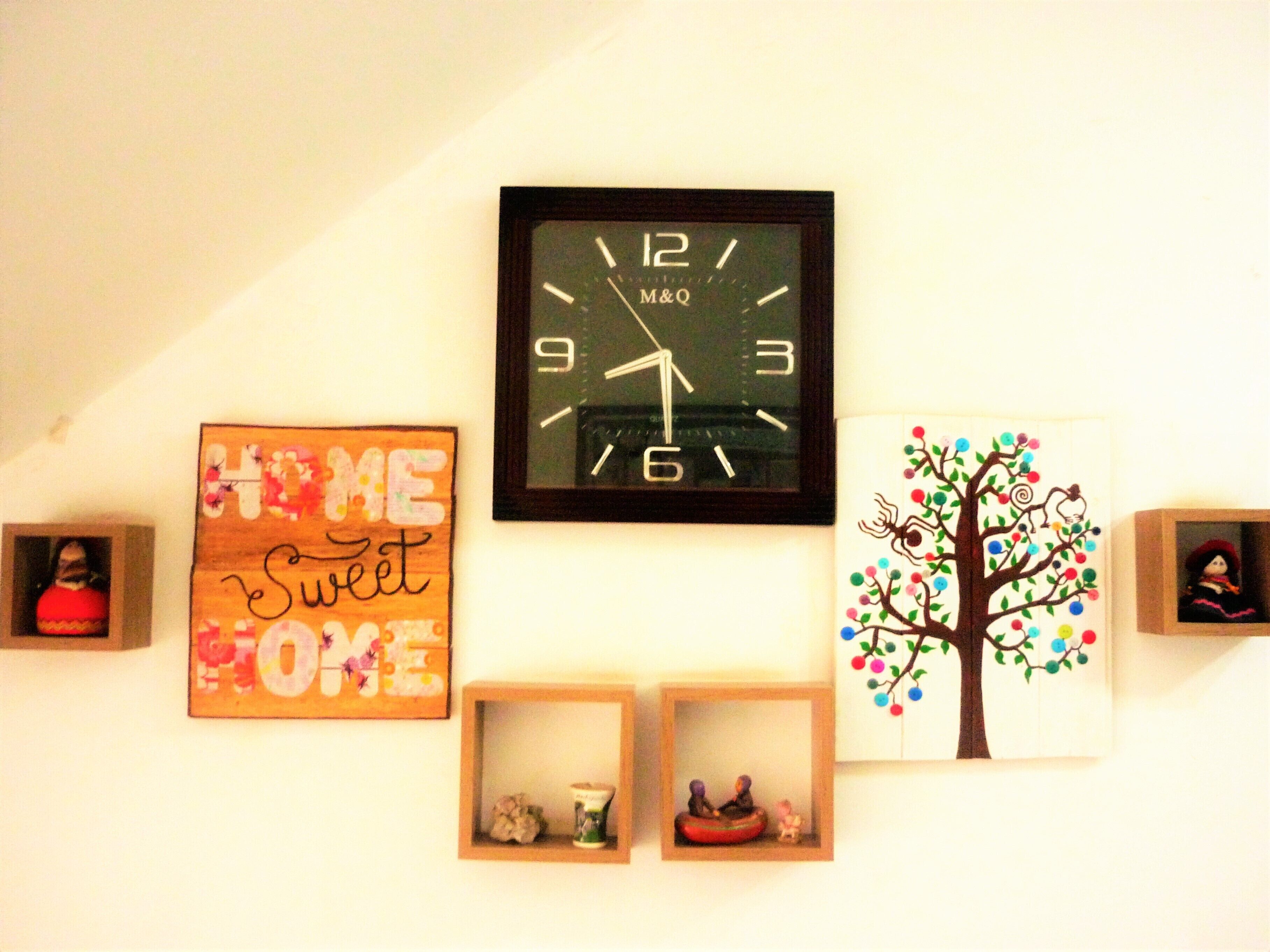 A wall with a clock, a sign saying "Home Sweet Home," and a decorative tree.