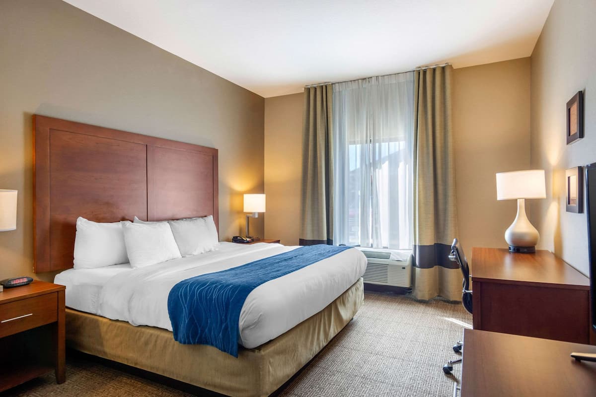 A hotel room with a large bed, two bedside tables with lamps, a desk with a chair, and a window with curtains.