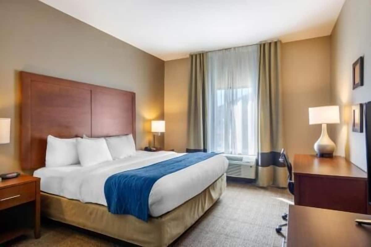 A hotel room with a large bed, bedside tables, a desk, and a window with curtains.