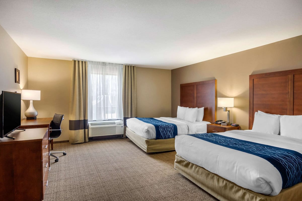 A hotel room with two beds, a desk with a chair, a TV, and a window with curtains.
