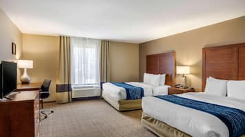 A hotel room with two beds, a desk with a chair, a TV, and a window with curtains.