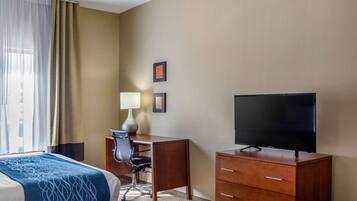 A hotel room with a bed, a desk with a chair, a television, and a lamp.