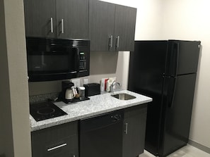 A compact kitchen with dark cabinets, a black microwave, a black refrigerator, a coffee maker, and a sink. - MainStay Suites Odessa I-20 (Odessa)