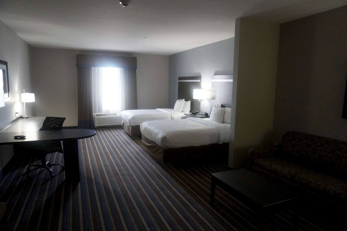 Habitación de hotel con dos camas, un escritorio, una silla, un sofá y un ventanal con cortinas.