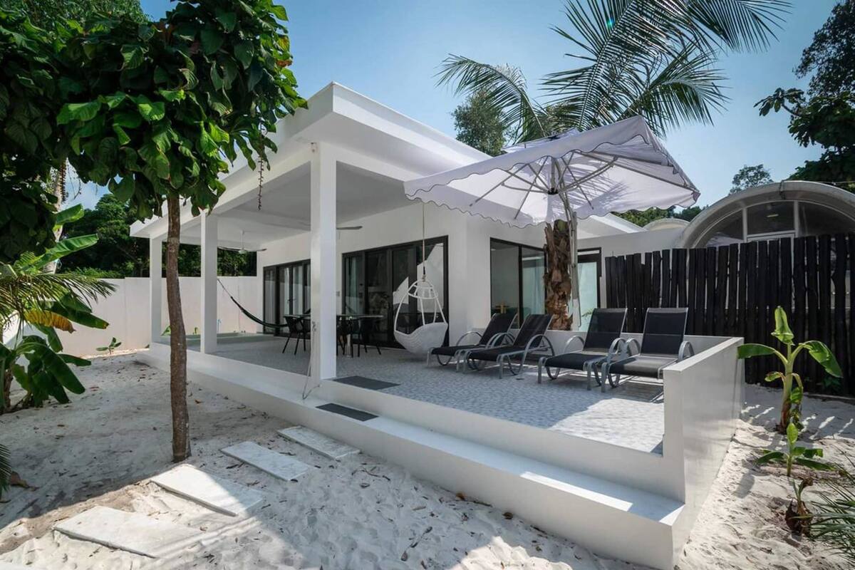 A modern outdoor lounge area with a white structure, seating, and an umbrella.