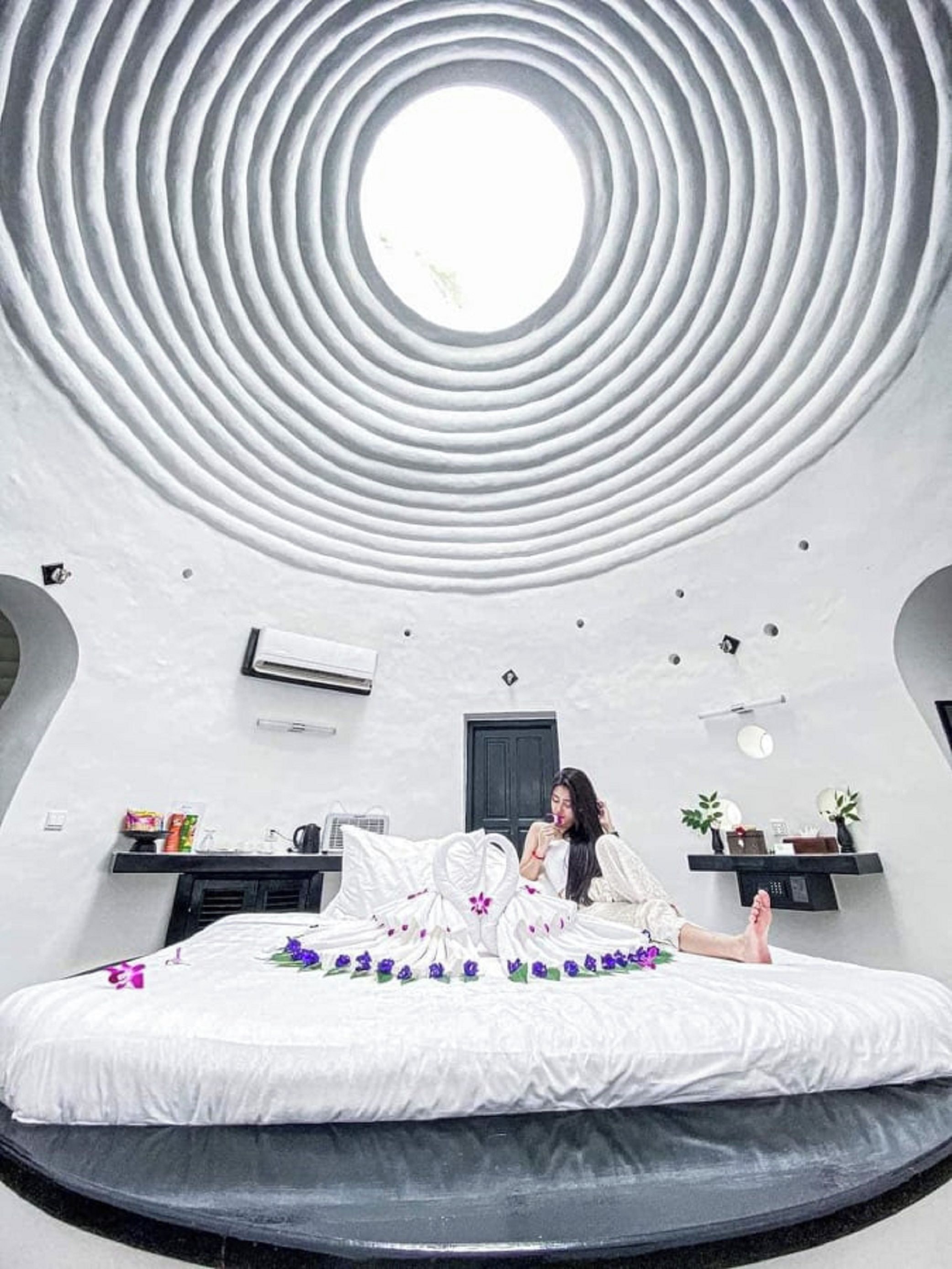 A modern bedroom with a circular ceiling design, a bed with a floral bedspread, and a small bedside table.