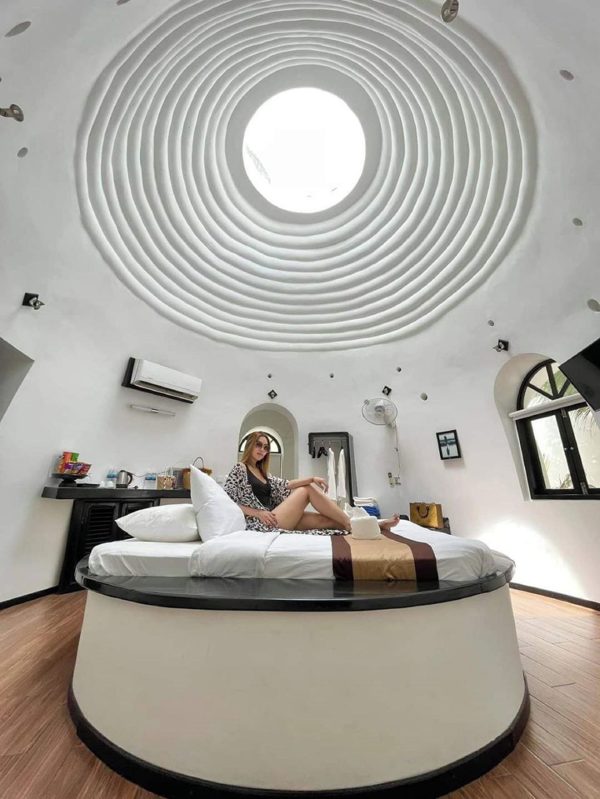 A circular room with a skylight, a bed, and a small table with items.