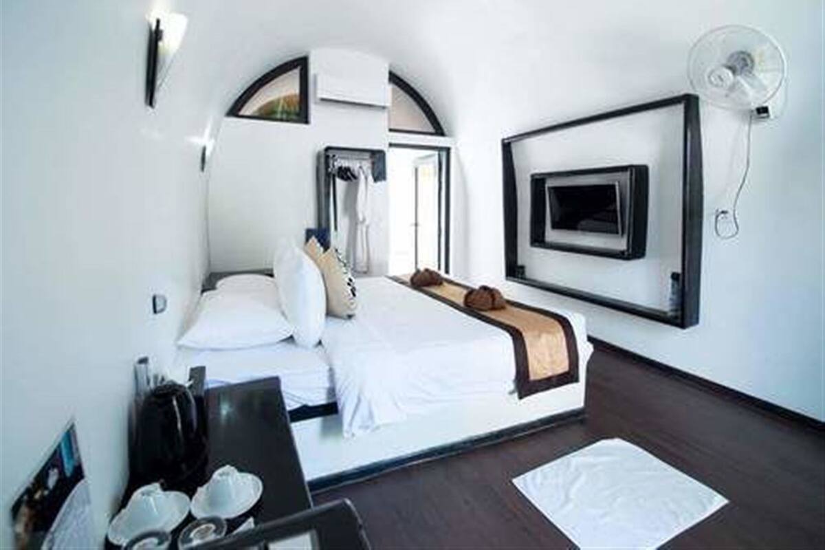 A hotel room with a bed, a desk, a TV, and a wall-mounted fan.
