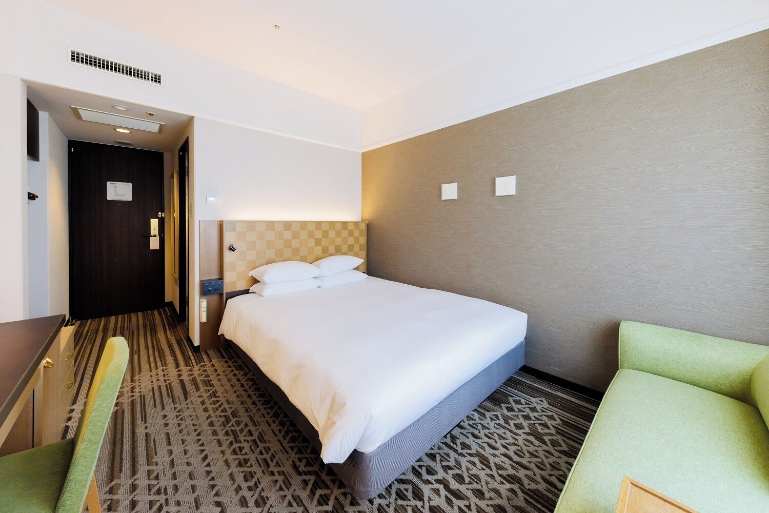 Una habitación de hotel con una cama grande, un escritorio y un sillón verde.