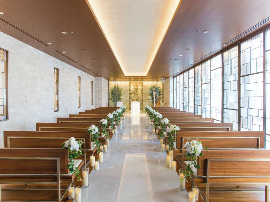 A church interior with wooden pews, a central aisle, and large windows.