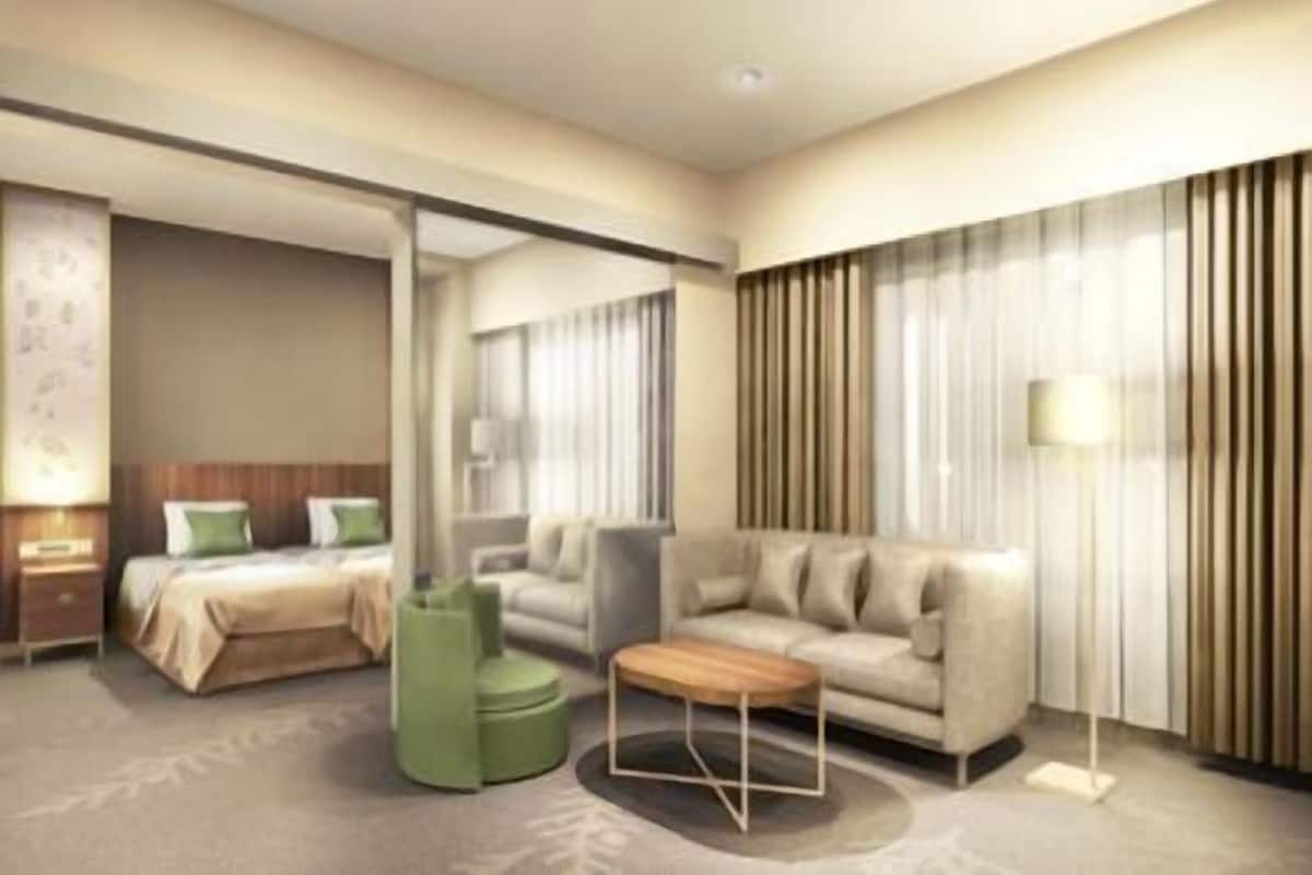 Una habitación de hotel moderna con una cama, un sofá, un reposapiés verde y una lámpara de pie.