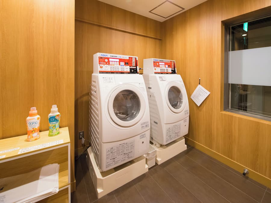 A laundry area with two stacked washing machines, a shelf with detergent bottles, and a window with a view.