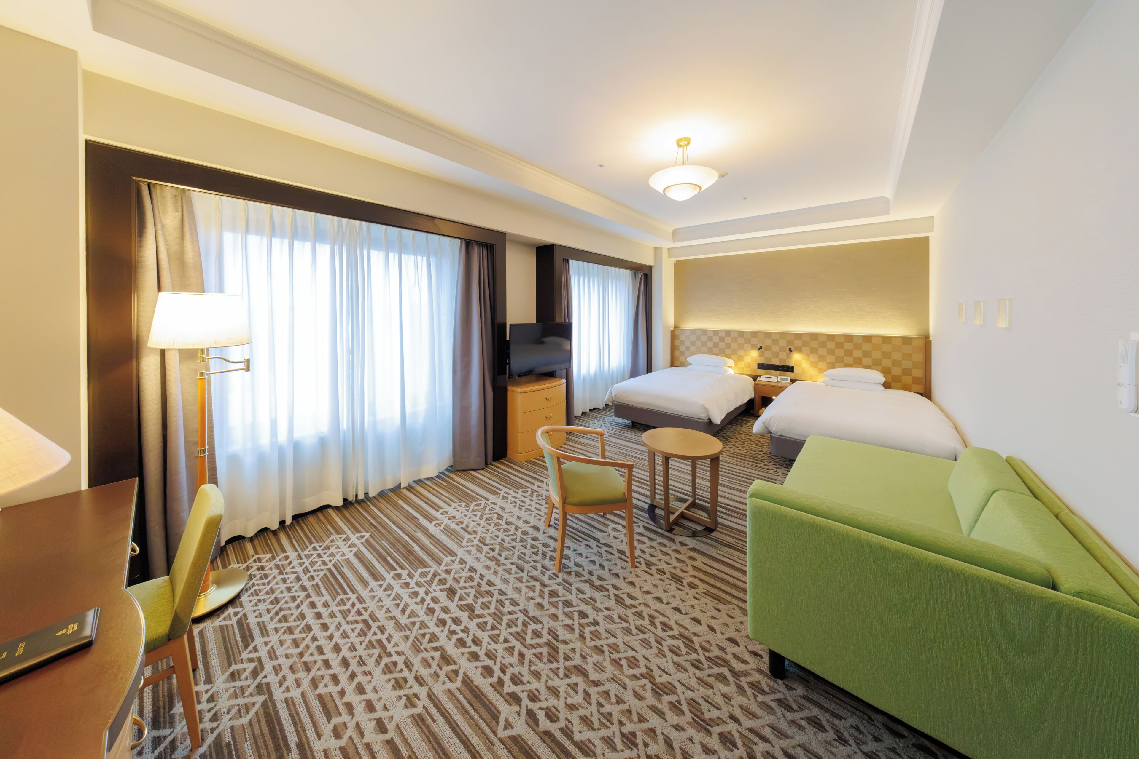 Hotellihuone, jossa on sänky, työpöytä, tuoli, pieni pöytä ja vihreä sohva.