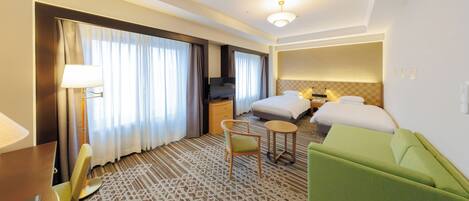 A hotel room with a bed, a desk, a chair, a small table, and a green sofa.
