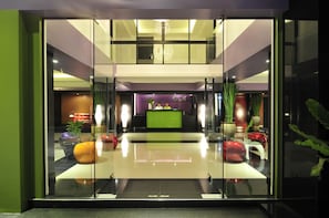 A modern lobby with a reception desk, glass walls, and decorative plants.