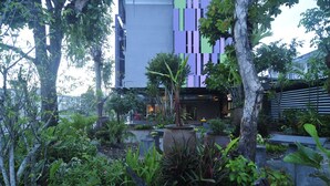 Un espace jardin agrémenté de diverses plantes et arbres, un coin salon avec des bancs, et un bâtiment à l’arrière-plan, doté d’une façade moderne.