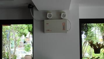 A room with a white ceiling, a wall-mounted air conditioning unit, and a window with a view of greenery outside.