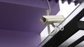 A surveillance camera mounted on a purple wall with a white cable.