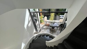 A spiral staircase leading to a patio area with a table and chairs, surrounded by greenery and a view of the outdoors. - Arthur&Paul - Caters to Men (Phnom Penh)
