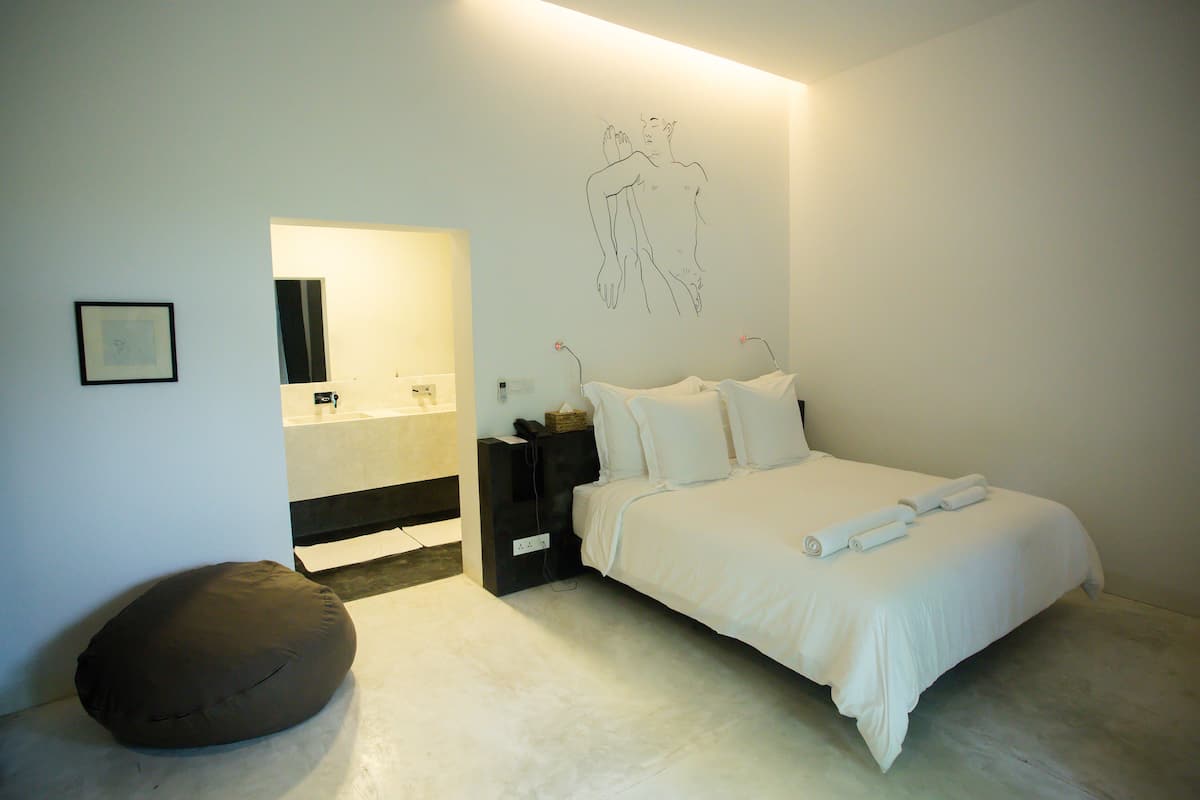 A bedroom with a bed, bedside tables, a bedside lamp, a wall-mounted artwork, a mirror, and a brown bean bag chair.